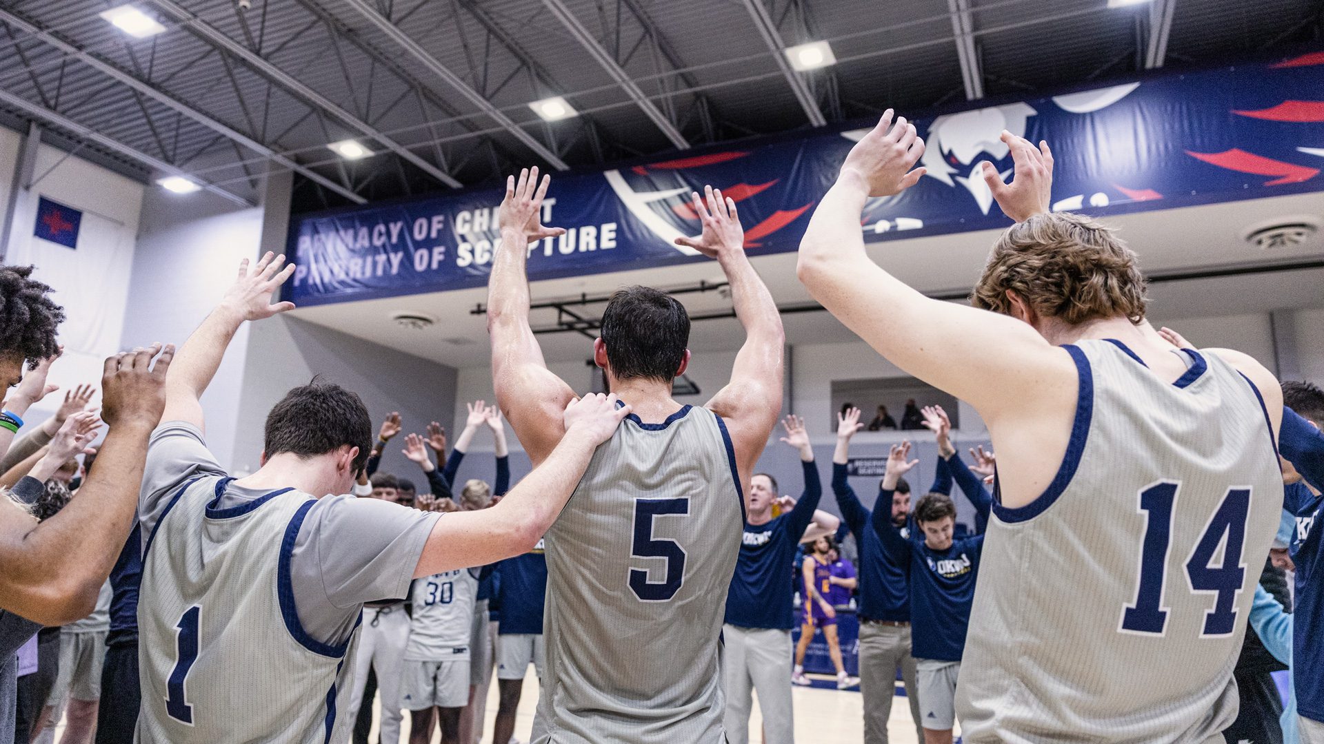 Photo of men's basketball players raising hands