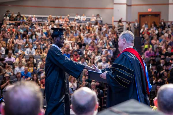 A student shaking Presiden Dunn's hand as they accept their diploma